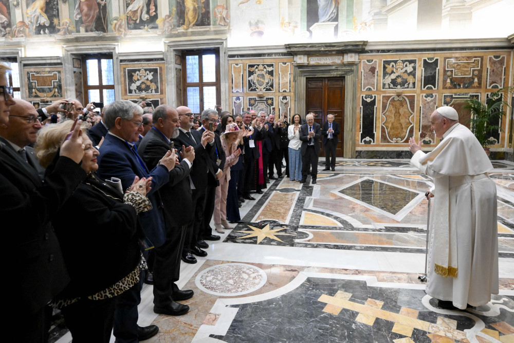 Pope Francis waves at an assembled crowd of lay people while using a cane inside