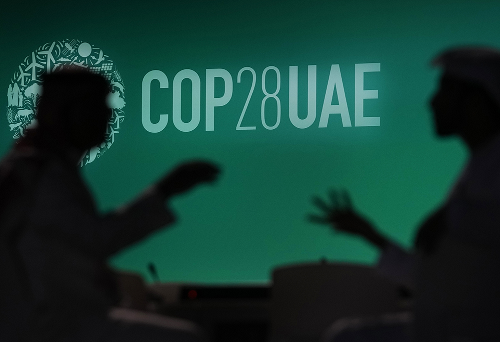 People are silhouetted against a logo for the COP28 U.N. climate summit, Nov. 29, in Dubai, United Arab Emirates. (AP photo/Rafiq Maqbool, File)