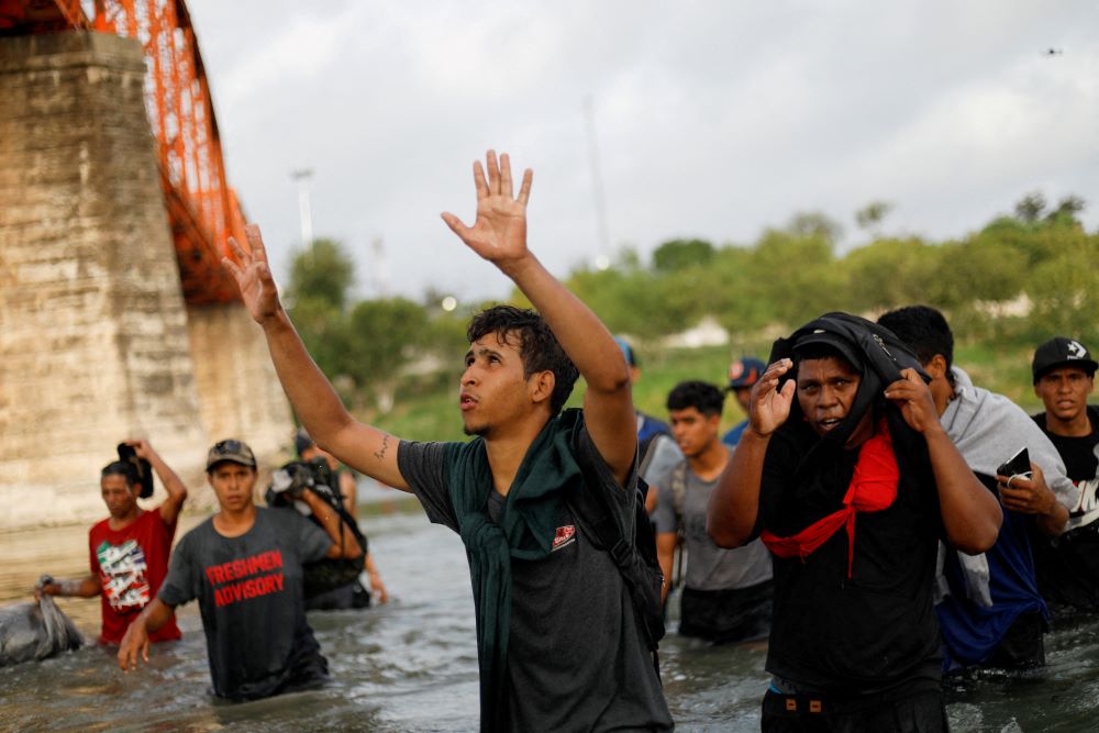 Several people stand in river. One man's hands are raised as if praising God. 