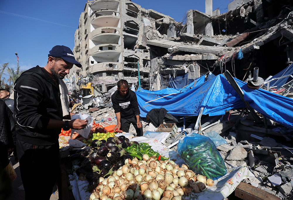 A Palestinian vendor prepares his products in an open-air market in the Nuseirat refugee camp in the central Gaza Strip Nov. 30 near the ruins of houses and buildings destroyed in Israeli airstrikes during the Hamas-Israel conflict, amid a temporary truce between Hamas and Israel. (OSV News/Reuters/Ibraheem Abu Mustafa)