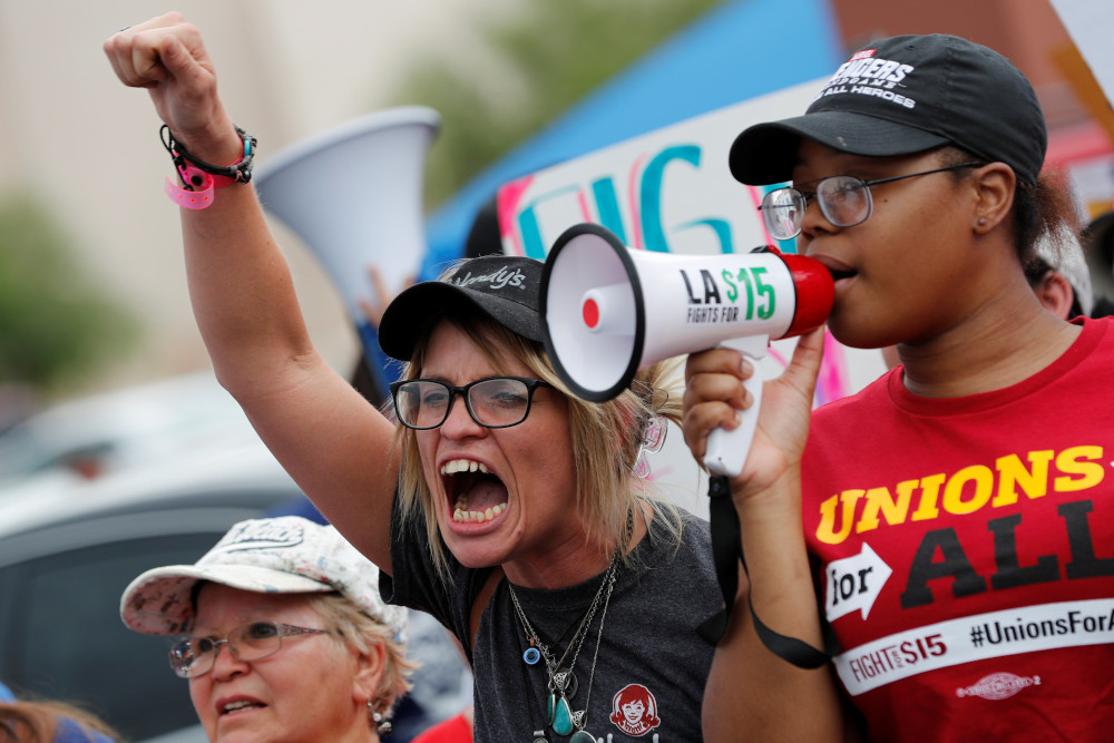 A crowd of people including a person holding a megaphone and a person with a fist raised gather