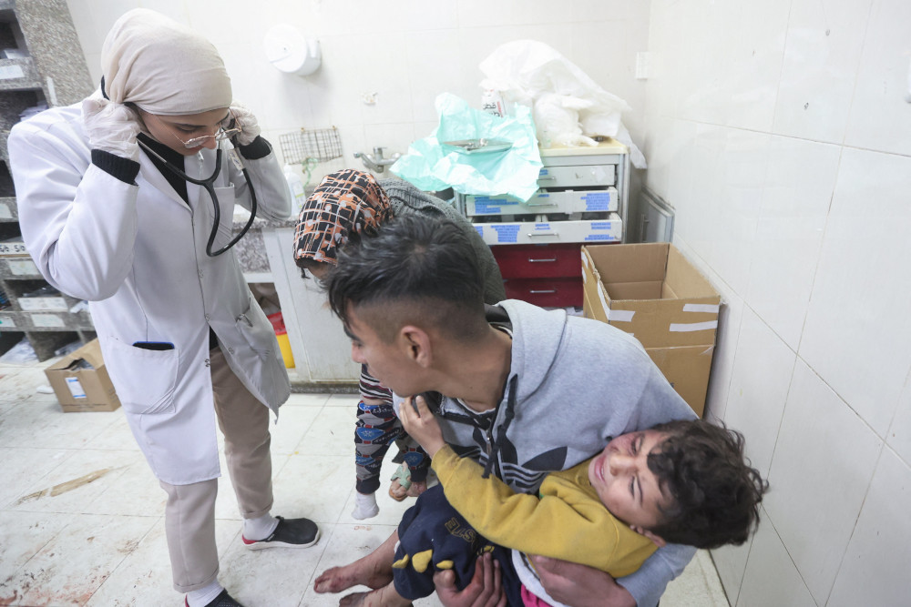 A person carries a child in distress to a medical professional. The floor of the facility looks stained, potentially with blood.