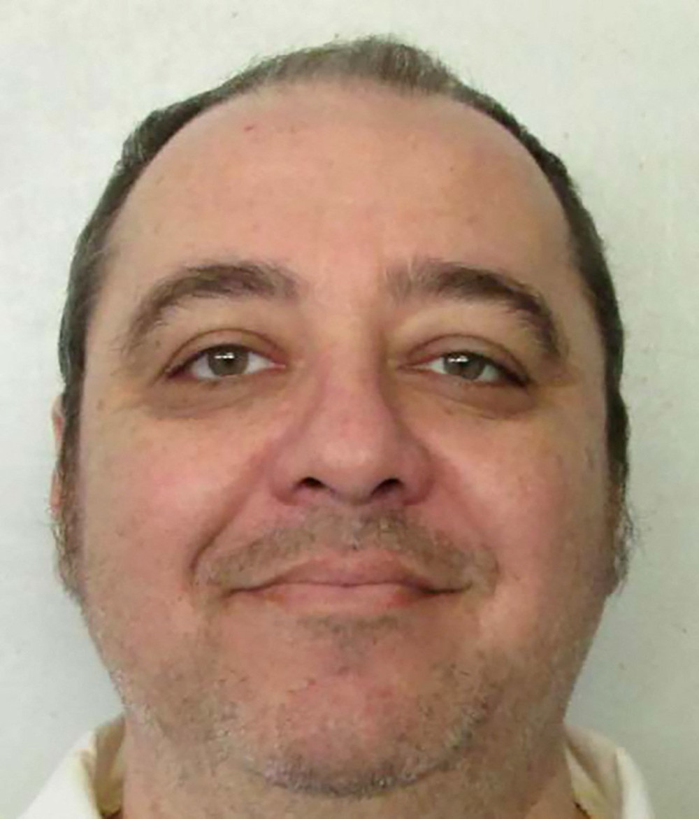 A headshot of a white man with brown, receding hair who smiles faintly at the camera.