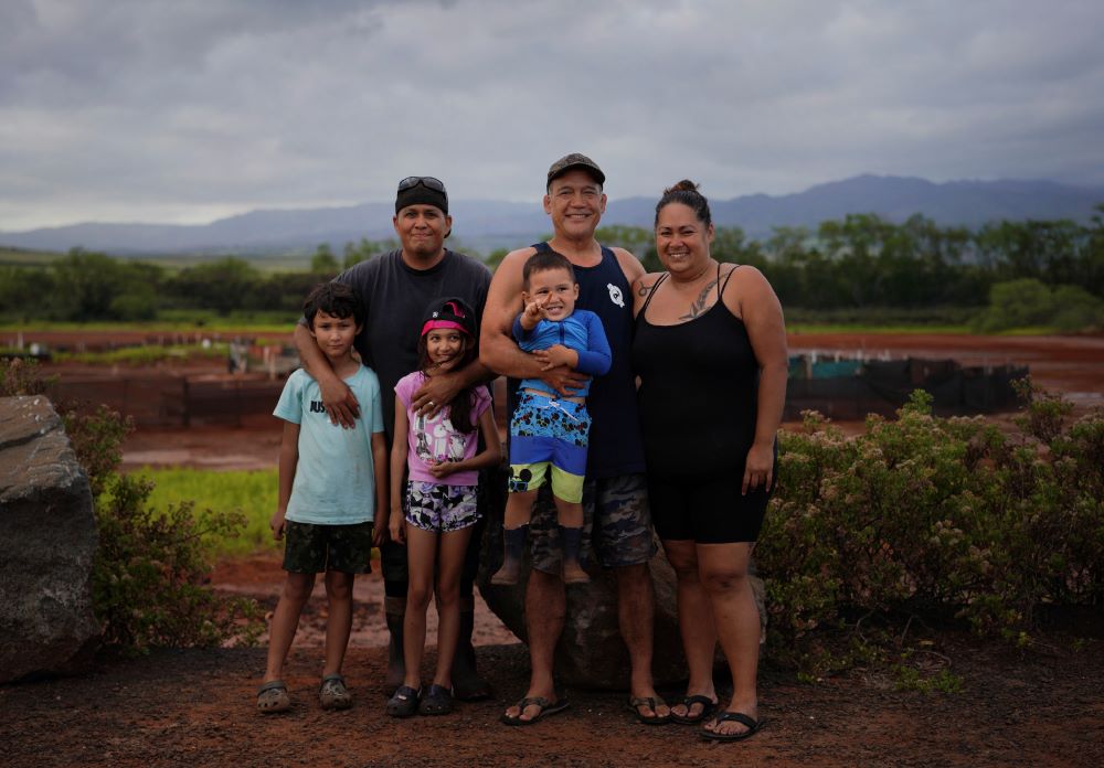 Kurt Kuali'i, father of Elijah Kuali'i and Arianna Kuali'i, stands with his fellow salt makers, Ivan Kaneko, Tanya Kaneko and their son Taivan Kaneko, for a portrait in front of the Hanapepe salt patch on Thursday, July 13, 2023, in Hanapepe, Hawaii. (AP Photo/Jessie Wardarski)