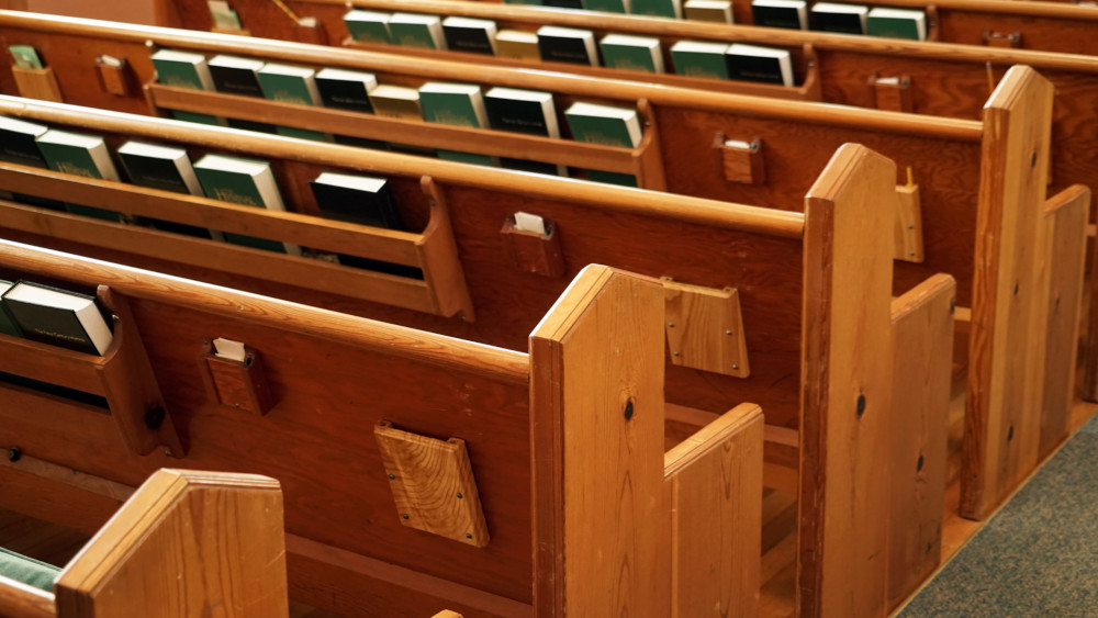 Empty church pews are visible from behind. There are hymnals and books in racks.