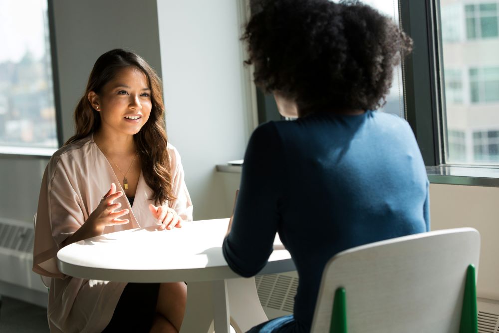 Two women sit across from each other at small table.