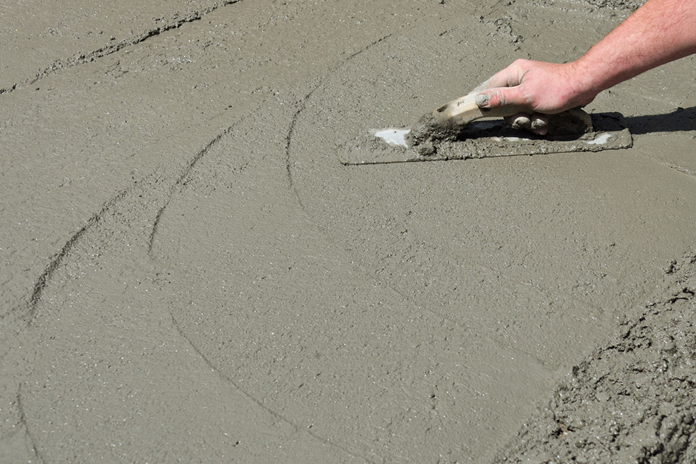 A hand with a trowel smooths newly poured concrete. (Dreamstime/Zigzagmtart)