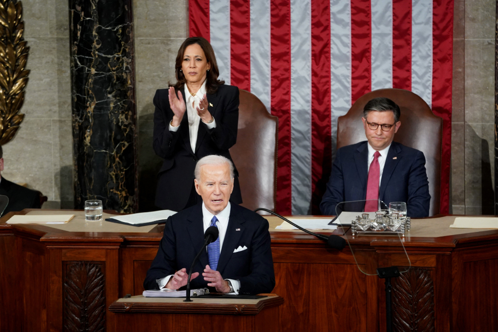 President Biden delivers State of the Union address on March 7, 2024. Behind him, Vice President Kamala Harris stands applauding, and Speaker of the House Mike Johnson sits listening. 