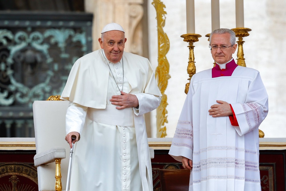 Pope Francis stands with cane smiling. 