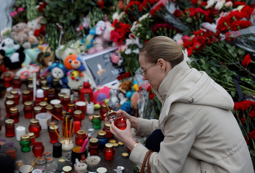 Woman lights candle at makeshift memorial