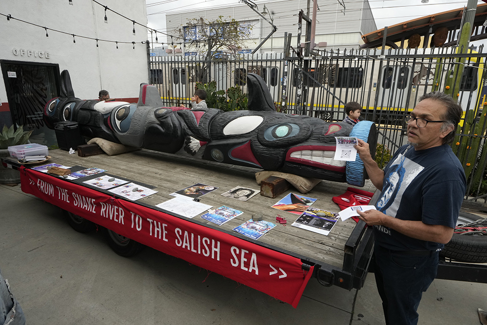 Freddie Lane, a member of the Lummi Nation who traveled from Washington State, with a totem pole touring across the country to stop the degradation of Native lands, joins members of the Apache Stronghold group gathered in the Los Angeles neighborhood of Boyle Heights at Self Help Graphics & Art paint protest signs on March 20, 2023. (AP/Damian Dovarganes, File)