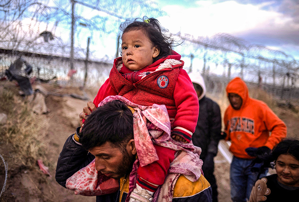 Briana, a 1-year-old migrant girl from Peru, is carried by her father, Jordan, as they search for an entry point into the United States past a razor wire-laden fence along the bank of the Rio Grande in El Paso, Texas, March 26. (OSV News/Reuters/Adrees Latif)