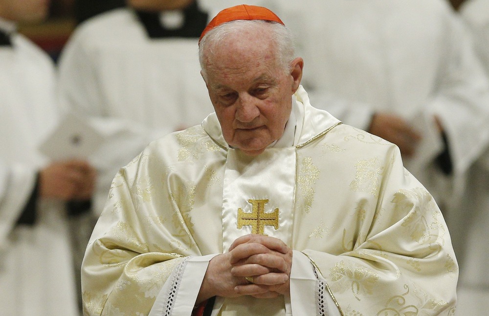 Prelate, vested, bows head and folds hands in prayer. 