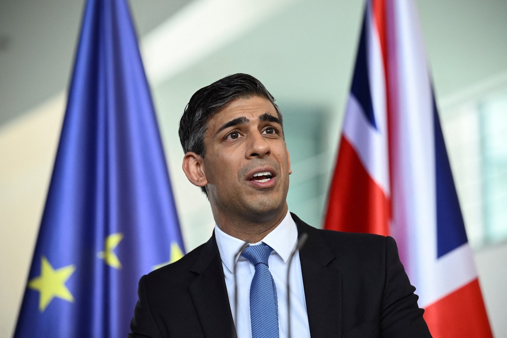 Prime Minister stands, pictured from the mid-waist up, before UK and EU flags