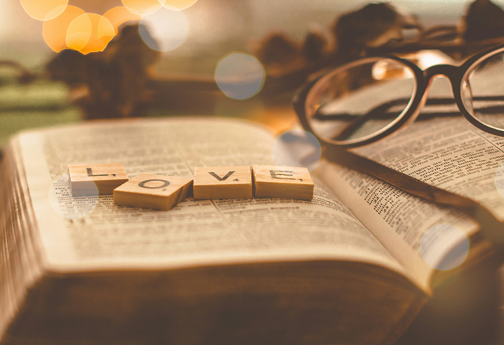 Letter tiles spell out the word "love" on top of a Bible laying open, with a pair of glasses next to the letters.(Unsplash/Emmanuel Phaeton)