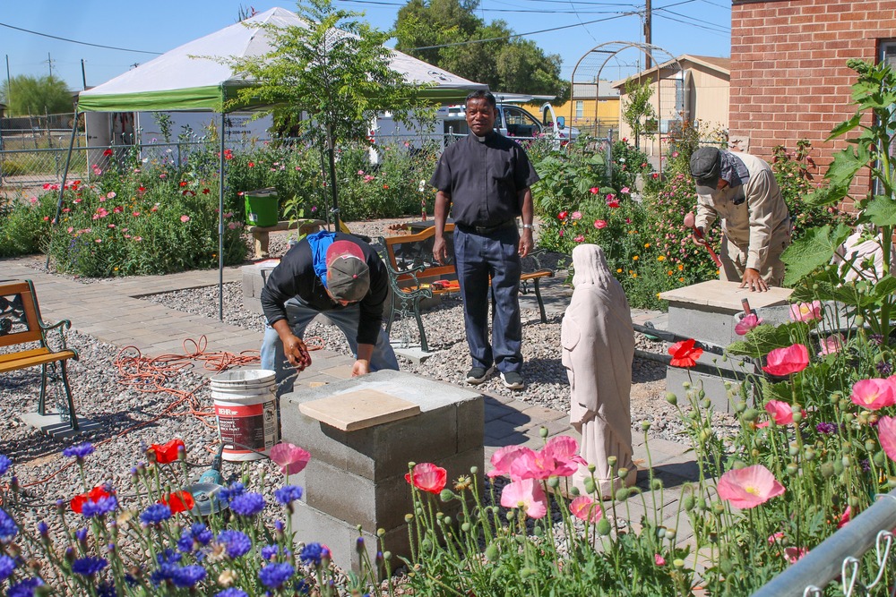 Priest and parishioners work in sunny garden.