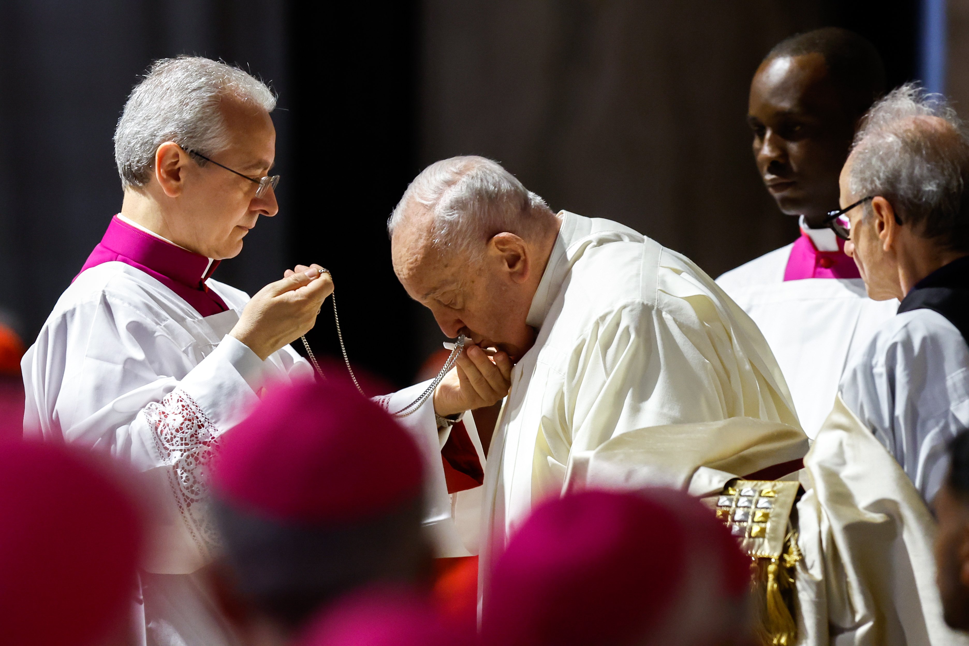 Pope Francis pictured in profile kissing pectoral cross held by aide. 