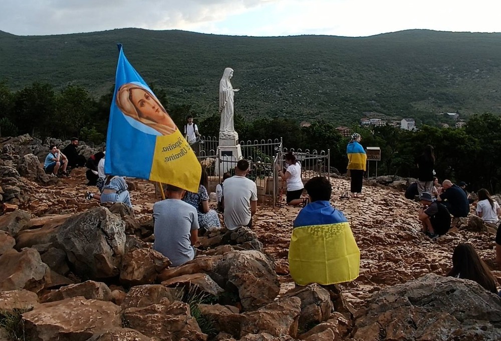 Children sit on rocky mound, draped in Ukrainian flags.