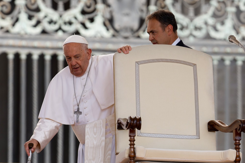 Pope Francis leans on cane as he prepares to sit. 