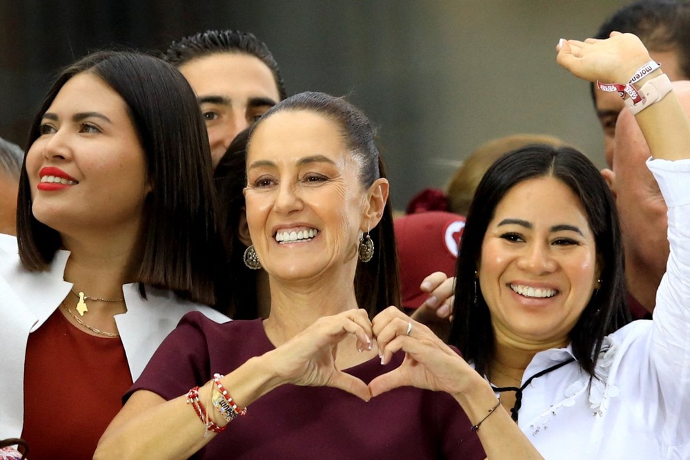 Scheinbaum smiles and makes a heart shape with her hands. 