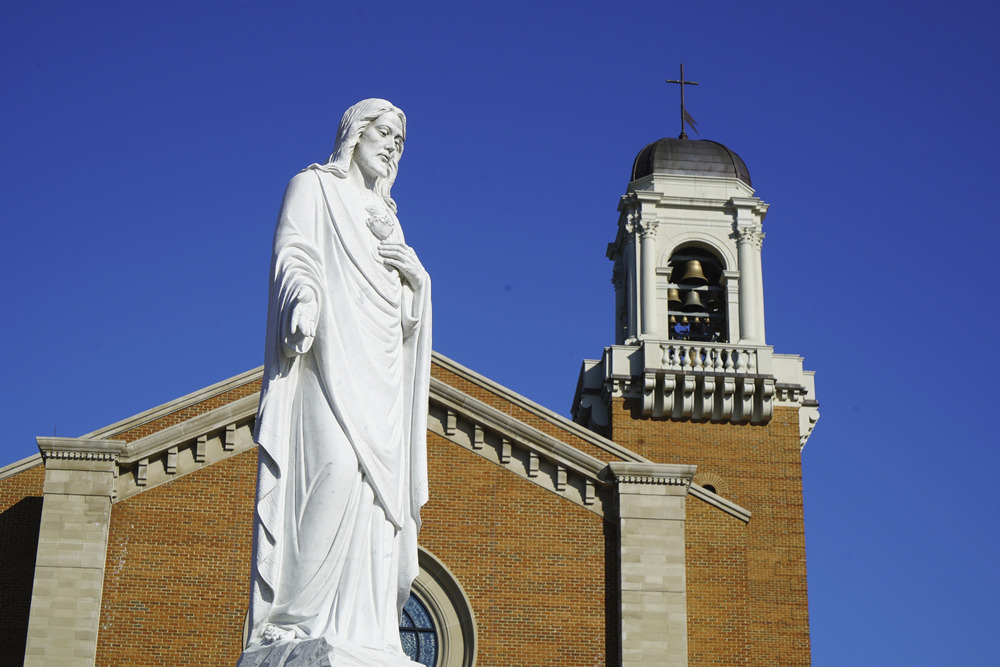 Diocese of Charlotte North Carolina fires gay teacher for his marriage Large statue of Jesus against cathedral's spire and blue sky