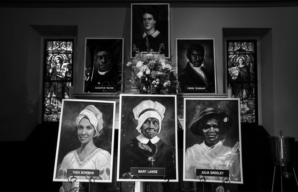 Black and white photo of the banners of the "Saintly Six" displayed in a church. 