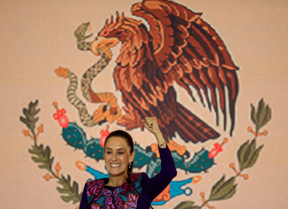 Bishop's congratulate Claudia Scheinbaum on her historic presidential victory. Scheinbaum smiles and raises fist in victory in front of banner bearing Mexico's eagle emblem.