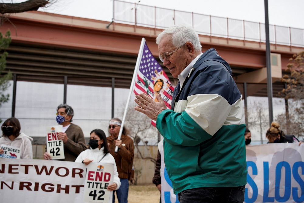 Garcia folds hand in prayer, supporters bearing banners seen in background