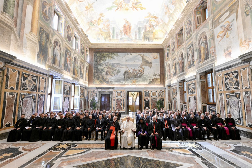 Pope sits flanked by other dignitaries, and backed by large assembly of conference participants. 