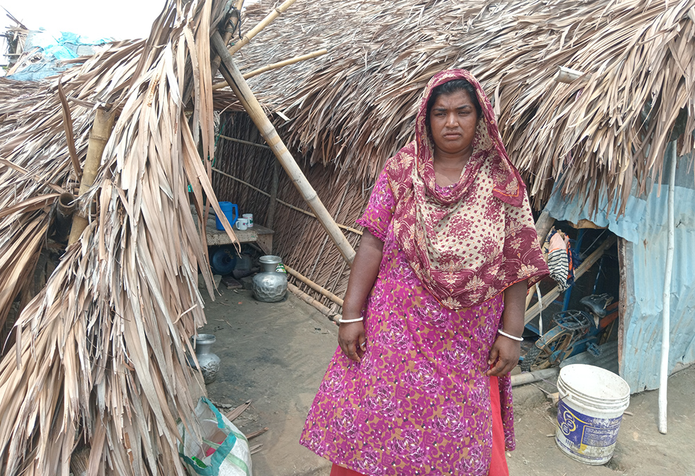 Chompa Das, 35, stands before her house that was damaged in the storm April 9. She has two children with her husband, a shoemaker. Das couldn't afford to repair their house. When Cyclone Remal struck on May 26, she and her family members found shelter in a nuns school, for which she expressed gratitude. (GSR photo/Sumon Corraya)