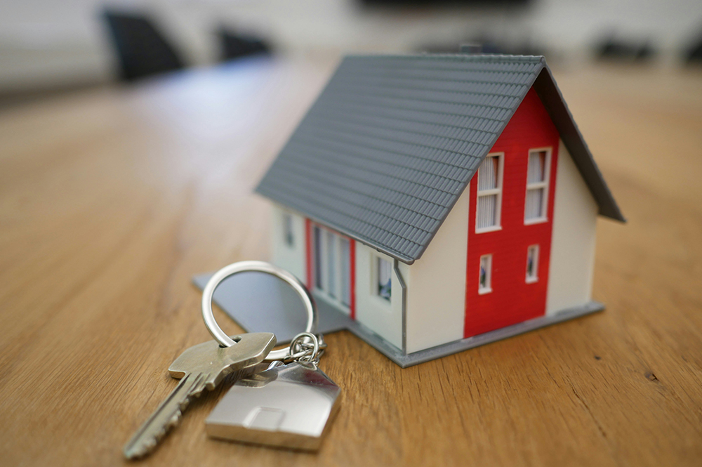 A set of keys on a table next to a toy house (Unsplash/Tierra Mallorca)