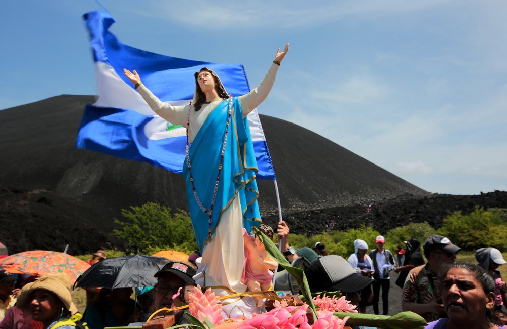 Statue of Mary and Nicaraguan flag stand above group of people.