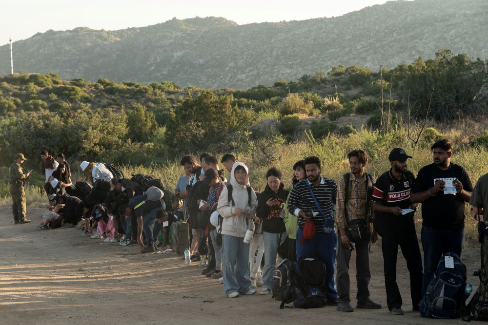 Asylum-seeking migrants stand in line to be transported at a staging area near the border wall, after U.S. President Joe Biden announced a sweeping border security enforcement effort, in Jacumba Hot Springs, California June 5. 