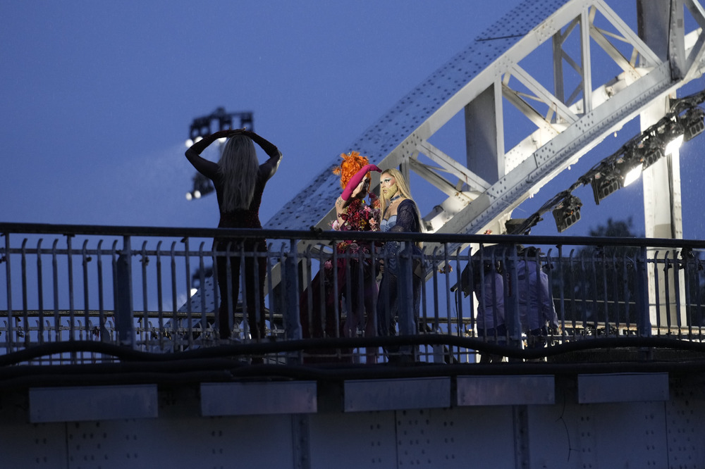 Drag queens on bridge at night, backlit by bridge's arch. 