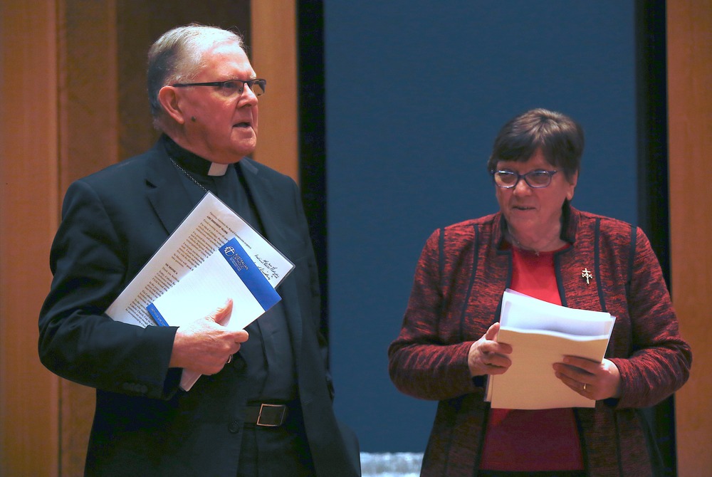 Coleridge and Cavanagh both standing, holding presentation materials. 