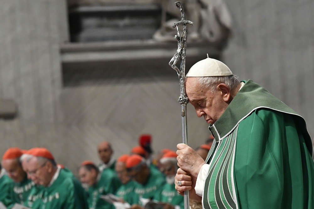 Francis, vested for ordinary time, leans head on crosier while praying. 