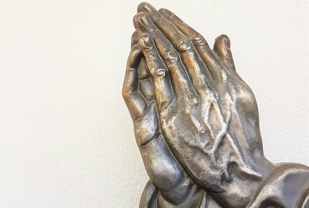 A bronze statue of hands clasped in prayer (Unsplash/Deb Dowd)