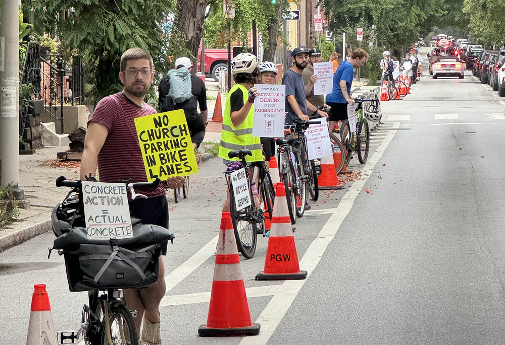 People with bikes and protest signs stand in a lane demarcated by traffic cones. 