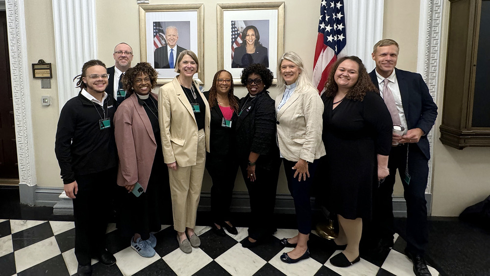 A group of nine people stands in front of America flag and portraits of President Joe Biden and Vice-President Kamala Harris. 