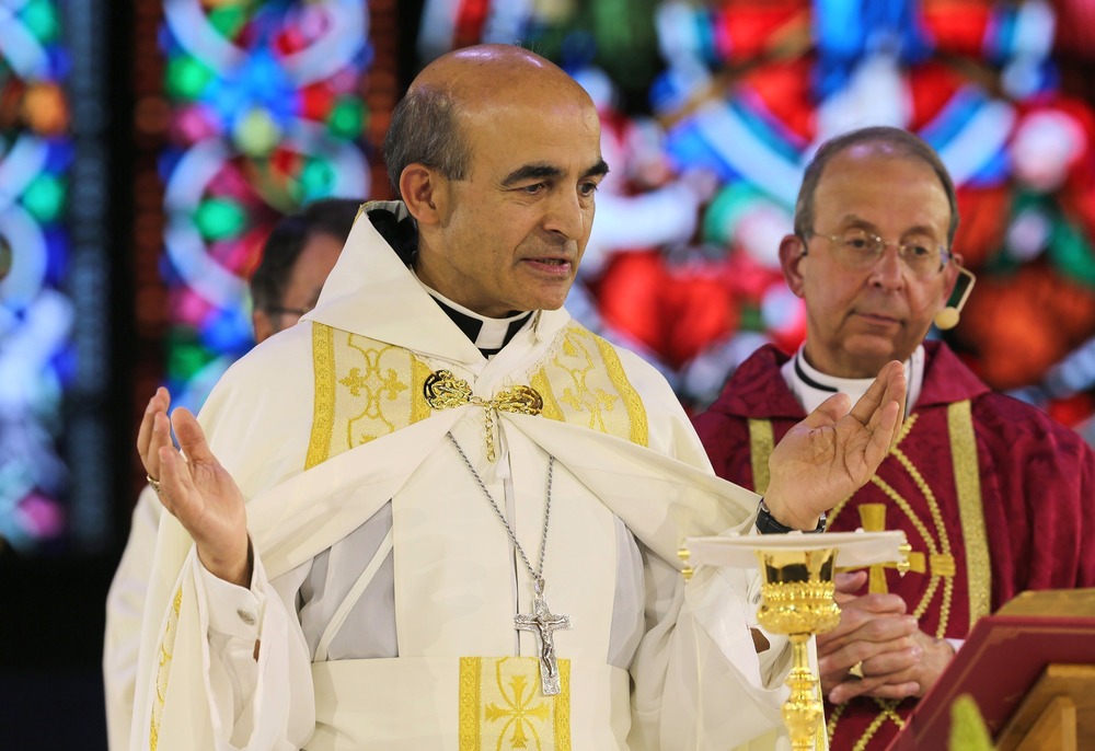 Zaidan, vested for Mass, raises hands in prayer at altar. 