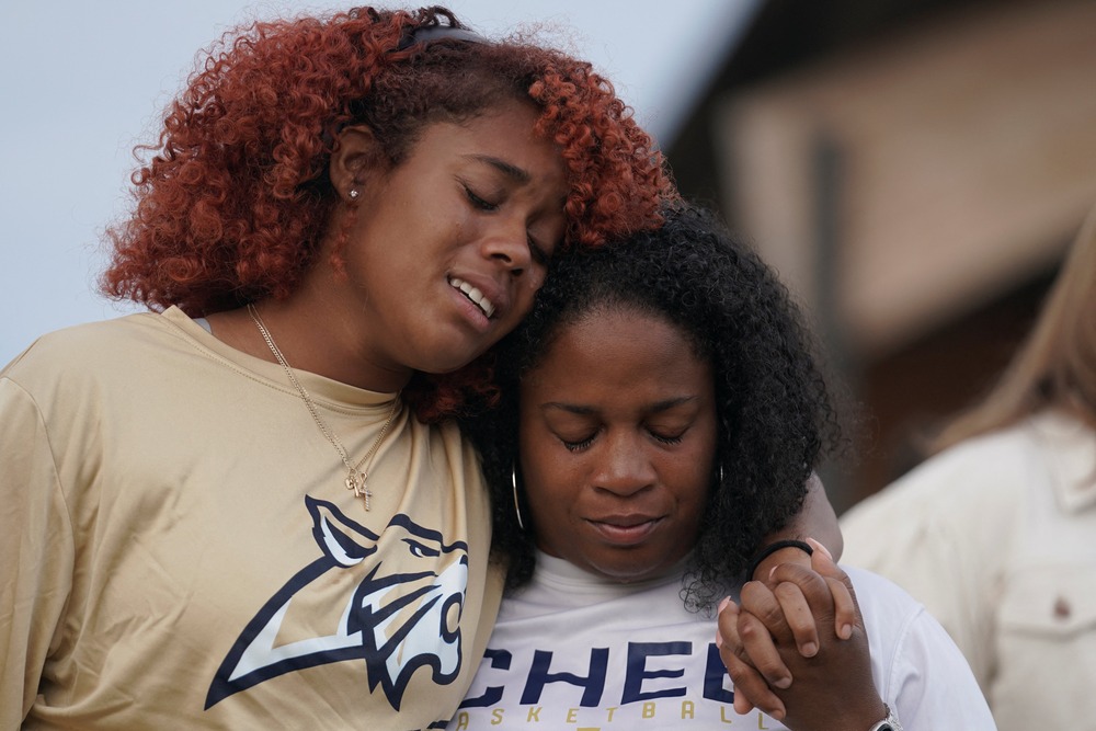 Two women stand side by side, one has her arm around the other. 