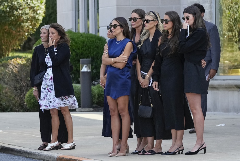 A group of women watching the hearse out of frame.