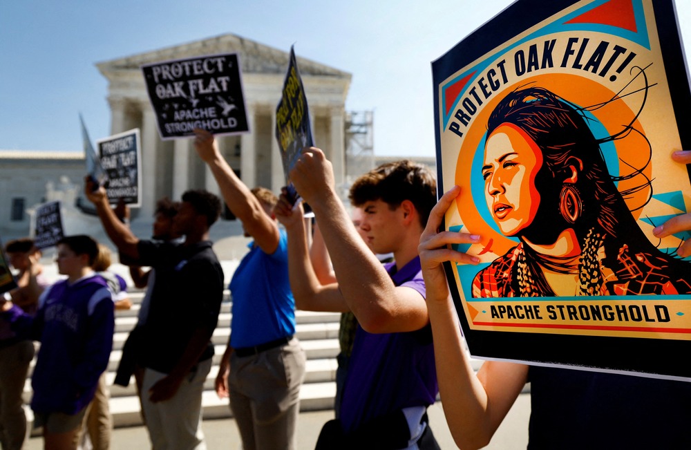 People stand holding signs in support of Apache Stronghold; Supreme Court building seen in background.