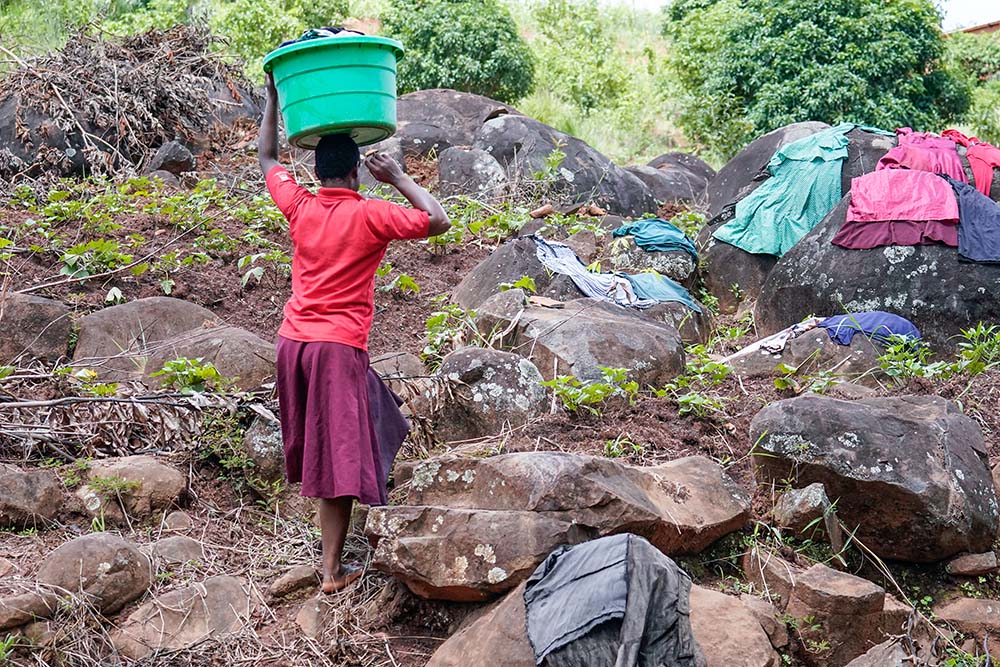 Clothes washed at the stream of Mpholiwa village in Malawi on March 15, 2022, dry spread out rocks or in the grass, as a girl waits to take them home afterward. (Courtesy of Monica Ichife)