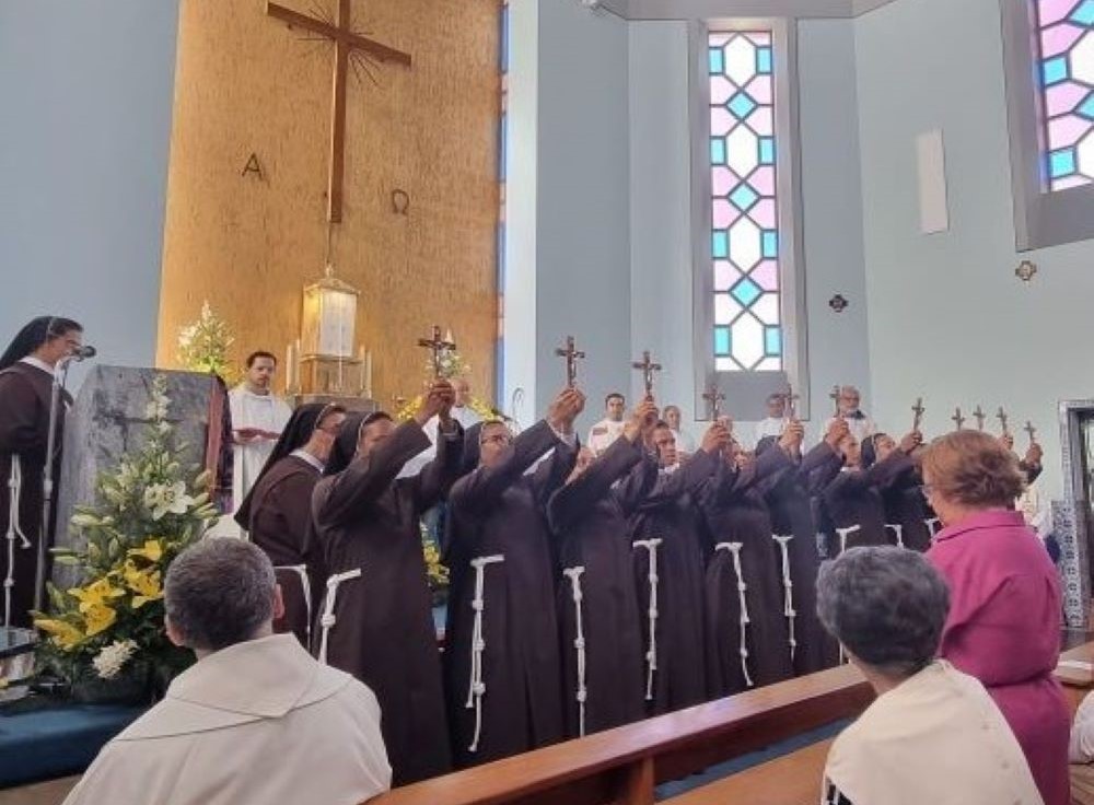 Sisters in brown habits hold up crosses while standing together on an altar. 