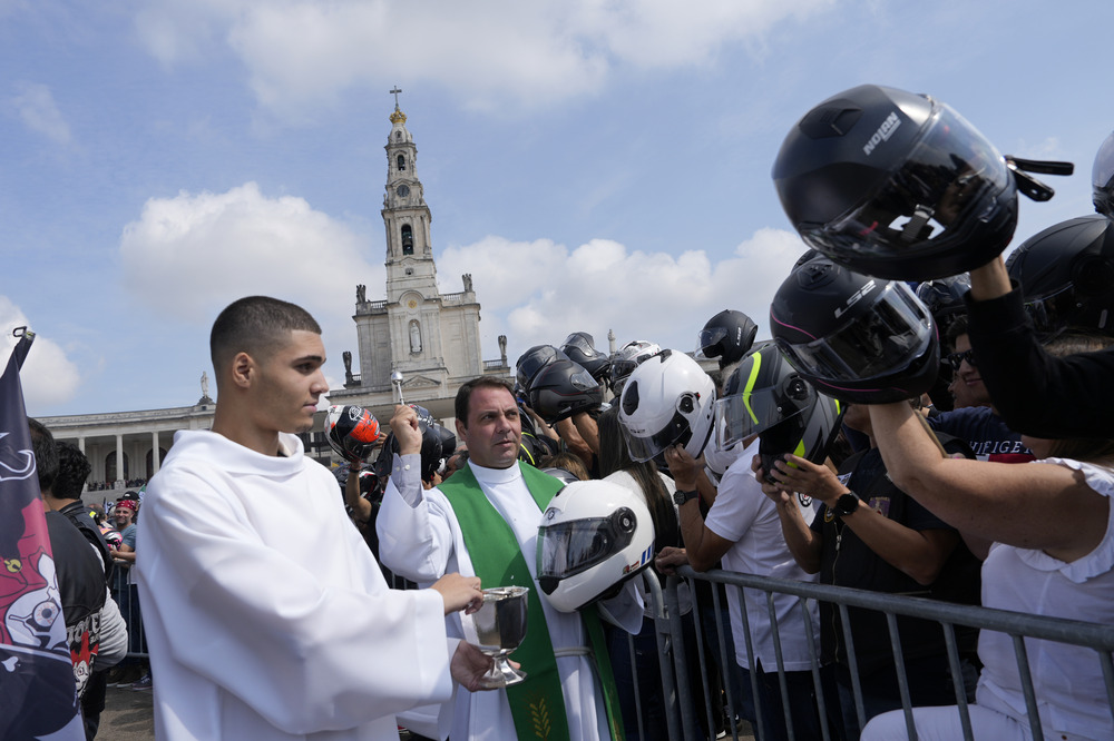 Blessing of Helmets, Fatima, Portugal, Sept. 22, 2024. Priest flings holy water and crowd of bikers holding their helmets up.
