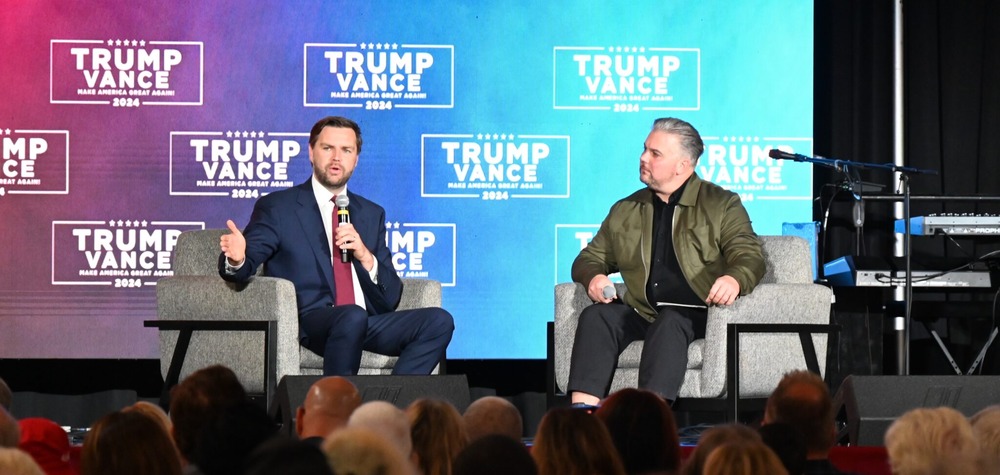 Vance and Howard sit side by side on a stage.