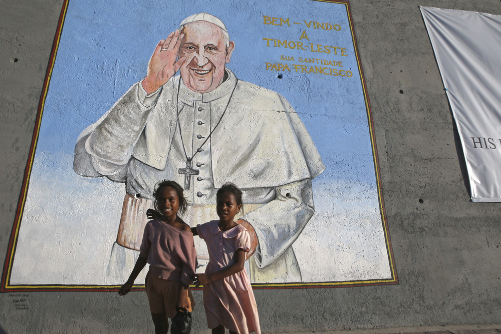 Two young children stand beneath large mural of Pope Francis.