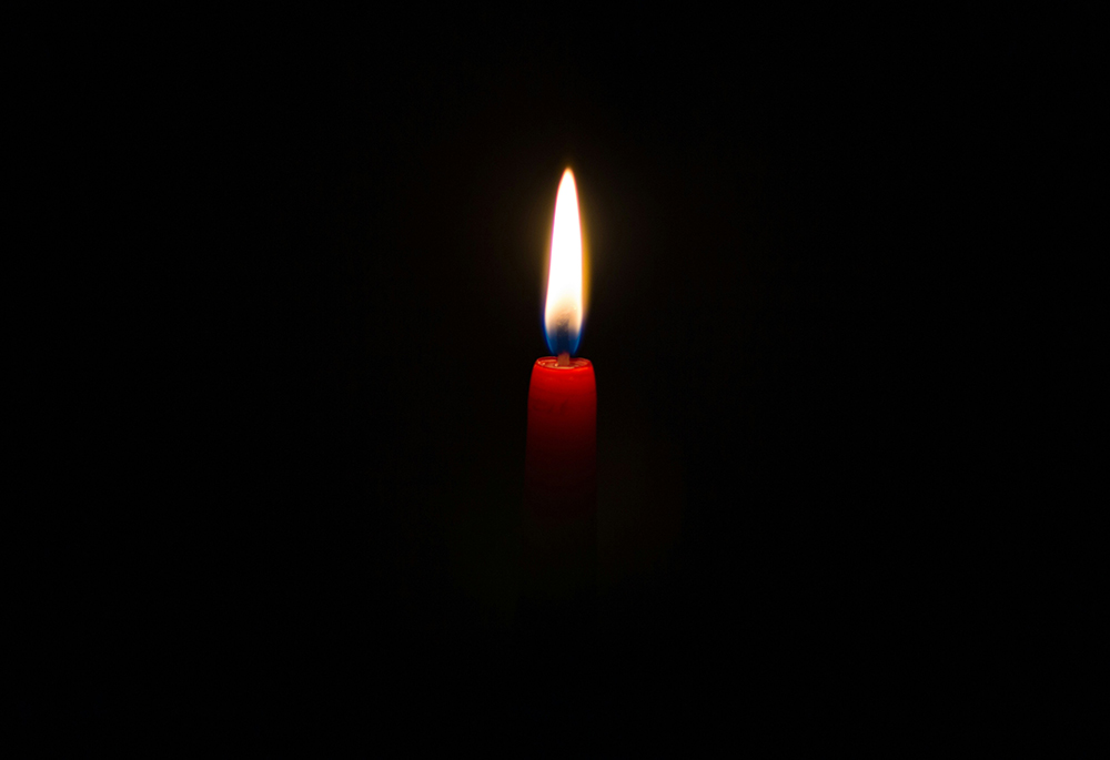 A candle burns amid darkness in a photo illustration. (Unsplash/David Monje)