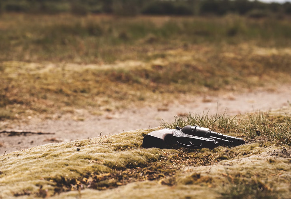 A pistol, possibly an antique, lies on the ground in an outdoor setting. (Unsplash/Jens Lelie)